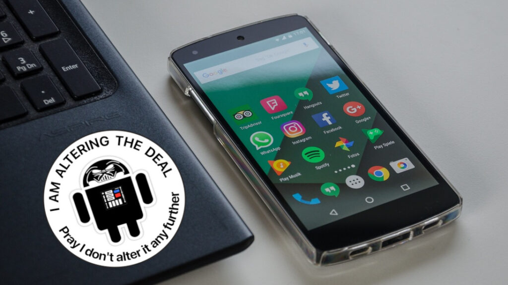 Smartphone auf einem Tisch neben einem Laptop. Auf dem Laptop ist ein Aufkleber "I am altering the deal – Pray I don't alter it any further"